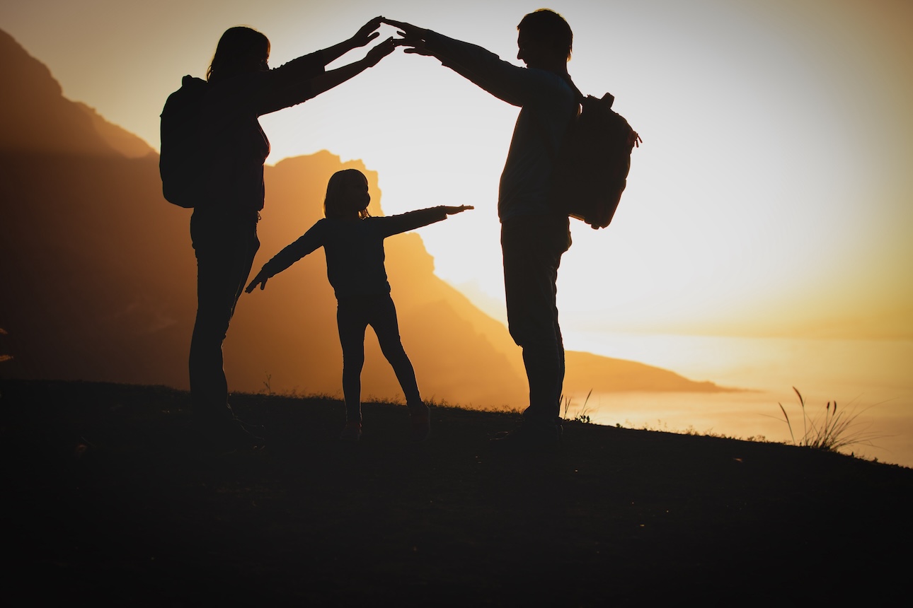 Silhouette of two adults and one youth against a sunset